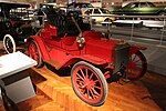 A red-colored, old-fashioned car with three seats and brass fittings