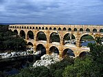 A stone aqueduct consisting of three levels with many arches crosses a river.