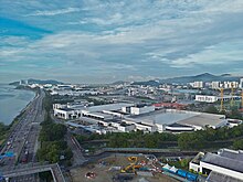 Aerial view of factories at an industrial zone in the city. An expressway lines the shore to the left of the zone.