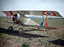 A white biplane fighter aircraft, siting in a field of dirt