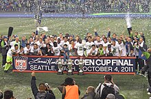 Several players are standing together with three trophies on the ground in front of them