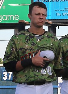 A man in a green baseball jersey and white pants