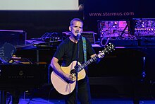 Photo d'un homme sur scène jouant de la guitare acoustique