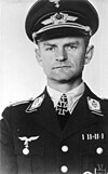 A man wearing a peaked cap and a military uniform with an Iron Cross displayed at the front of his uniform collar.