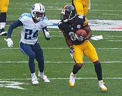 Un joueur de football américain balle sous le bras, pourchassé par un adversaire.