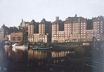 Fotografiet till vänster togs 1925 av Gustaf W. Cronquist på en autochromplåt och visar Stadsgårdens bebyggelse närmast Slussen. Här skedde stora förändringar i stadsbilden tills nästa bild som togs år 2010. Det enda huset som känns igen är det så kallade Sjömansinstitutets hus från 1914 som skymtar längs ut till vänster. Resten av bebyggelsen utgörs av de båda KF-husen. Det äldre är en ombyggnad från början av 1930-talet av det stora röda tegelhuset till höger som byggdes för Kooperativa förbundet mellan 1909 och 1912. Det nyare, även kallat "Glashuset", uppfördes på 1970-talet på platsen för bland annat Drottsgården.