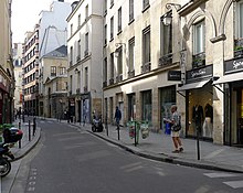 Rue plutôt étroite d’un quartier historique de Paris, avec quelques commerces.