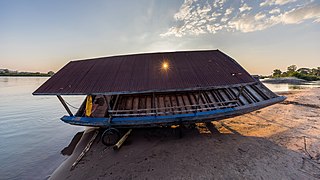 Carénage d'une pirogue sur la pointe d'une plage de sable au bord du Mékong sur l'île de Don Puay, Si Phan Don, Laos, avec des rayons de soleil filtrés à travers un trou dans son toit de tôle usé par la corrosion. Novembre 2019.