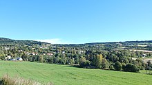 Aufnahme einer hügeligen Landschaft, die teils bebaut und teils bewaldet ist und teils Wiesen hat