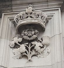 Photographie d'une sculpture d'un trèfle, d'une rose et d'un chardon sur une façade.