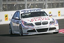 Voiture blanche de face, un virage, dans un circuit en ville, sur une piste sèche.