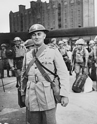 A military officer in a dress uniform with helmet standing on a quayside