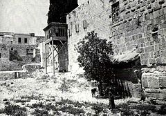 a black and white photograph showing a patch of rough ground with a stone wall running along the right side and a series of stones sticking out at the bottom of the wall in the foreground, partially obscured by a shrub