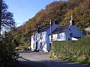 white-painted pub below wooded escarpment