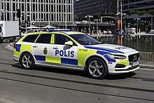 Das Bild zeigt einen modernen Kombi-PKW der Marke Volvo mit eingeschaltetem Blaulicht, Markierungen und Beschriftung der schwedischen Polizei.