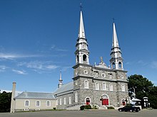 Photo d'une église grise avec deux hautes pointes et aux portes rouges.