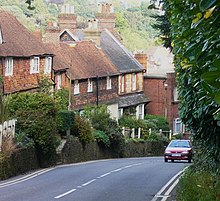 steep road with car passing a row of old red brick and tile-hung cottages