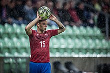 Sous la pluie un homme lève le ballon des deux bras au ciel, sans doute pour jouer une touche.