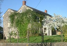 Gray stone building with slate roof, partially obscured by trees.