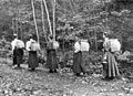 Four women walking in a line through a path in a forest, carrying pack baskets