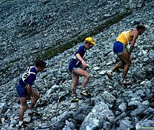 Trois coureurs grimpant dans un pierrier, les mains posées sur les cuisses.