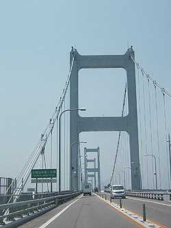 来島海峡第一大橋。"ステイロープ"とは写真手前左側の道路標識の後ろに見える垂直ではなくハの字に伸びる2本のロープ。その"ロッド"とはロープ下端の写真に映る白い筒状のものの更に下にある。破断したのは"センター"つまり中央支間のもの[72]。