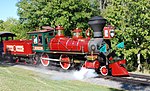 A red steam locomotive with a 4-4-0 wheel arrangement (four leading wheels, four driving wheels, and no trailing wheels) and its tender