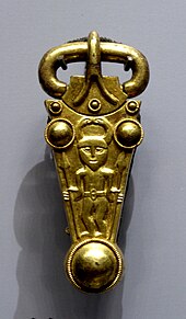 A gold buckle decorated with a man in a horned helmet carrying a spear in each hand.