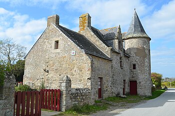 Vue d'une habitation en pierre grise, une tour avec toit conique et un portail rouge en premier plan.