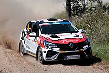 A small white-and-red car with a five door body is driven at speed along a gravel road.