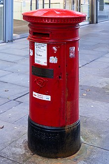 Boîte cylindrique rouge avec une base noire. Une petite plaque dorée est accroché au centre de la boîte.