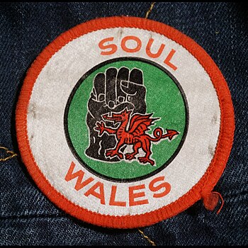 Ffotograff o fathodyn o'r 1970au gyda dwrn du symbol 'Black Power' a'r ddraig goch o fewn cylch gyda'r geiriau 'Soul Wales'