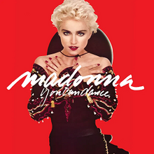 Madonna with short, blond hair, wearing a black dress, with her hands folded against her breasts and standing in front of a red background. She has a Spanish hat attached to her neck.