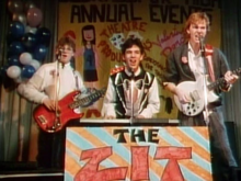 Three young men with musical instruments performing on stage. On the left is the bassist, in the centre is the keyboardist, and on the right is the guitarist.