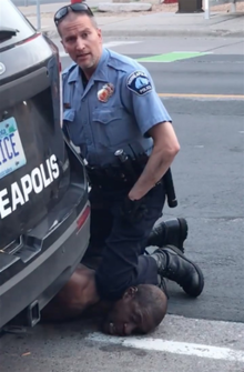 Police officer Derek Chauvin stares into the camera as he kneels on the neck of George Floyd, who is lying on his stomach on the street