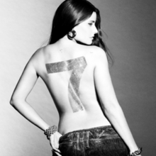 A black-and-white photograph of Furtado, shirtless and turned away from the camera, with a number 7 painted on her back.