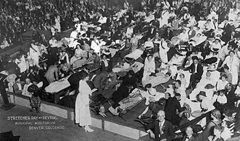 Stretcher Day at Revival in Municipal Auditorium at Denver , Colorado, 1921. The event attracted a capacity crowd of 12,000 attendees. People were carried in on cots, stretchers, chairs and beds; and awaited McPherson to pray over them for healing.