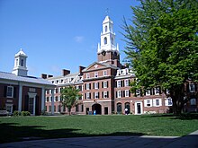 A college courtyard; a large brick building with a tall white spire is visible to the right