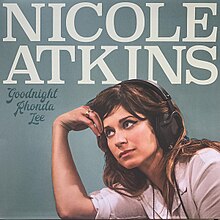 The teal cover features a brunette woman wearing a white shirt and black headphones, leaning on her right hand. The artist's name appears above the woman colored in white, and the album title is below the artist's last name.