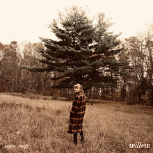 A sepia toned picture of Taylor Swift standing in a field. The background consists of trees.