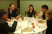 five of the main actors sitting around a dinner table