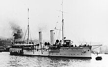 A large warship with a light gray hull moored off shore