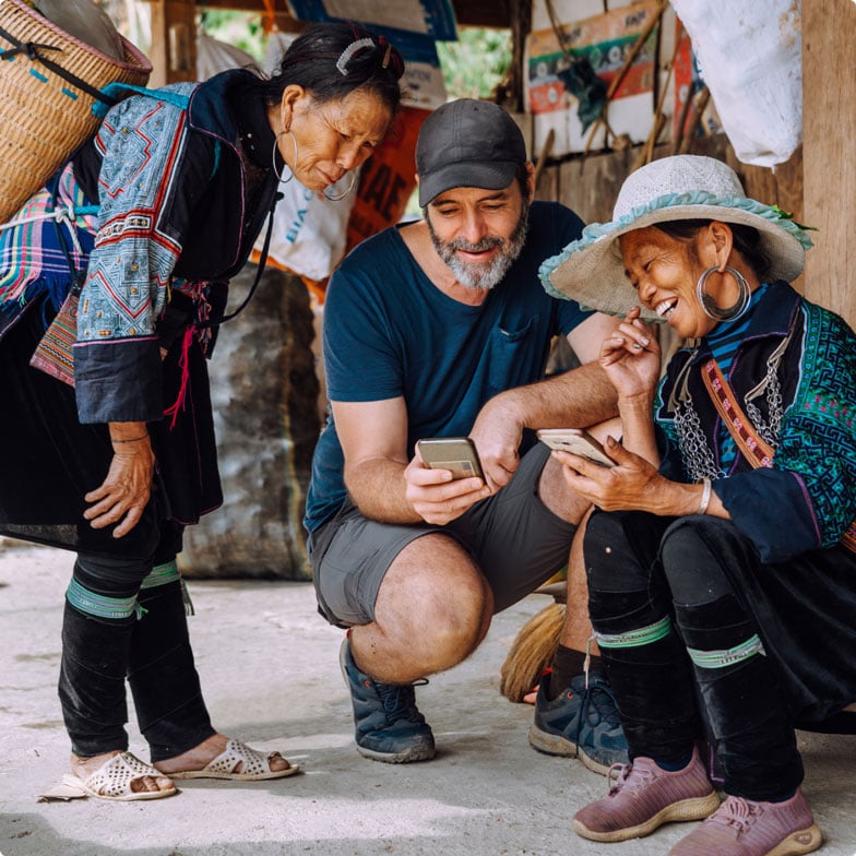 A Western man crouching down showing his phone to locals in South East Asia