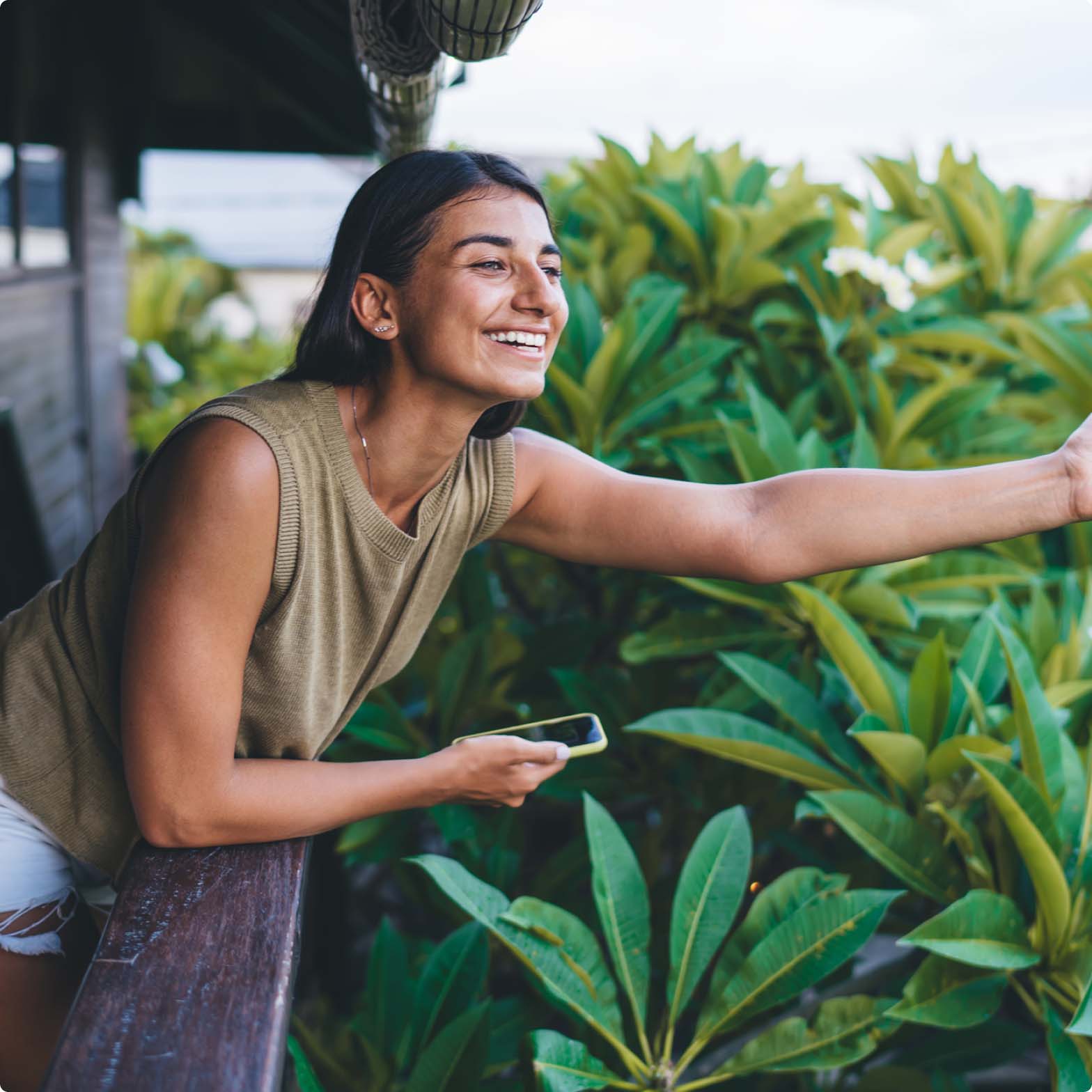 A woman reaching over a balcony surrounded by green foliage