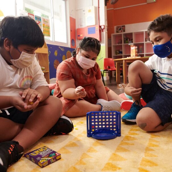 Children wear face masks and play with toys in a classroom-type setting