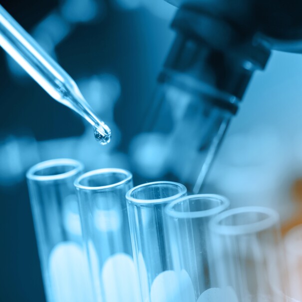 A microscope, test tubes, and a pipette with a drop of liquid emerging.