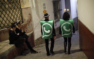 Revellers dressed up as dancers of 'Black Swan' check their mobile phones next to revellers dressed up as a Whatsapp logo as the