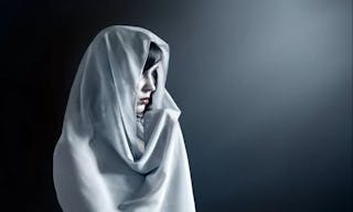 Young attractive woman in a veil prays on a dark background.