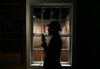 The curator of the exhibition "Sherlock Holmes: The Man Who Never Lived and Will Never Die" poses with a deerstalker hat and a s