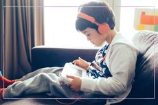 A young boy sat on a sofa playing a computer game